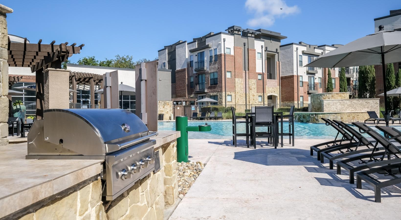 Relax and unwind poolside a pool with tables and chairs by it and buildings in the back